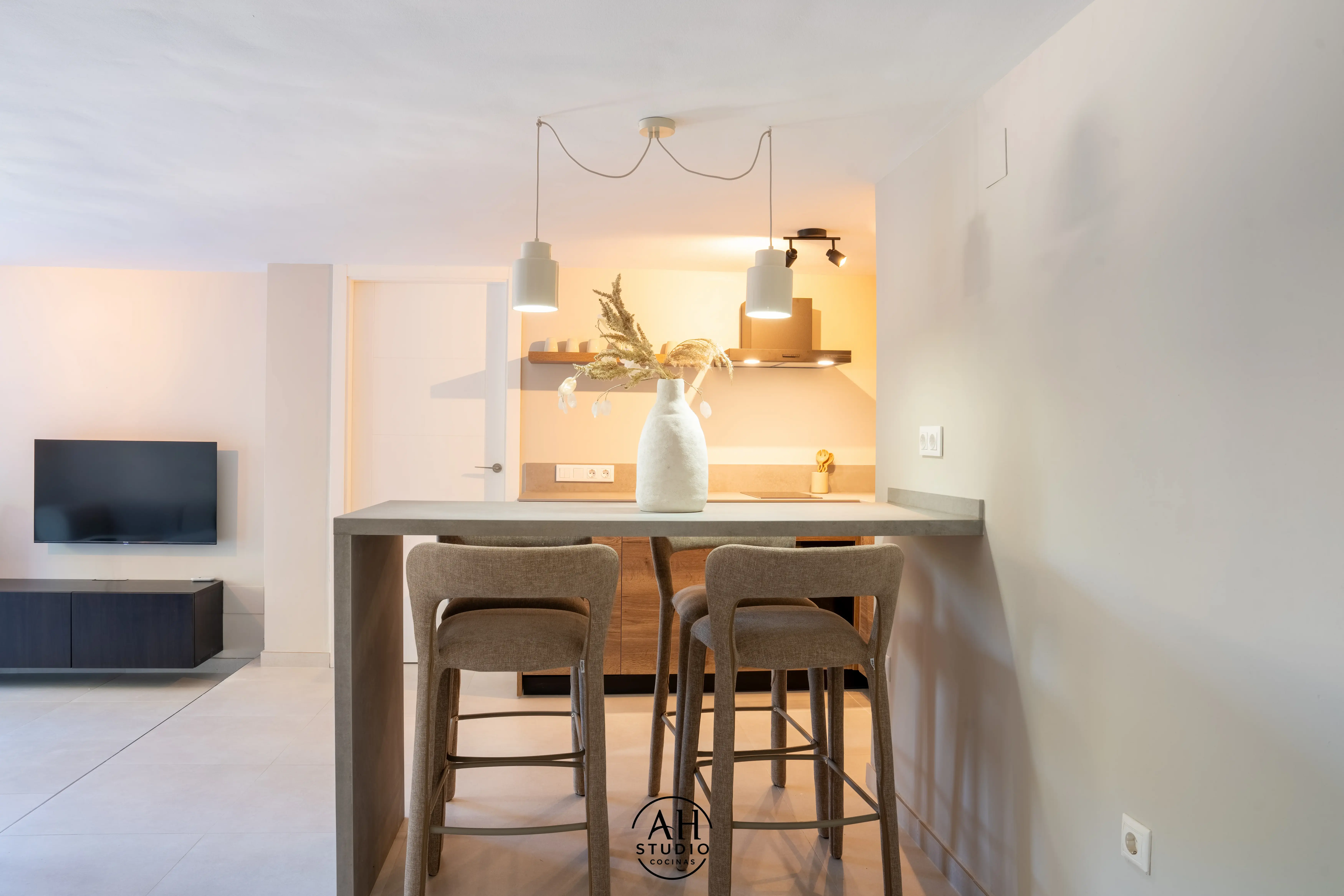 Barra de cocina con taburetes, lámparas colgantes y cocina de madera al fondo