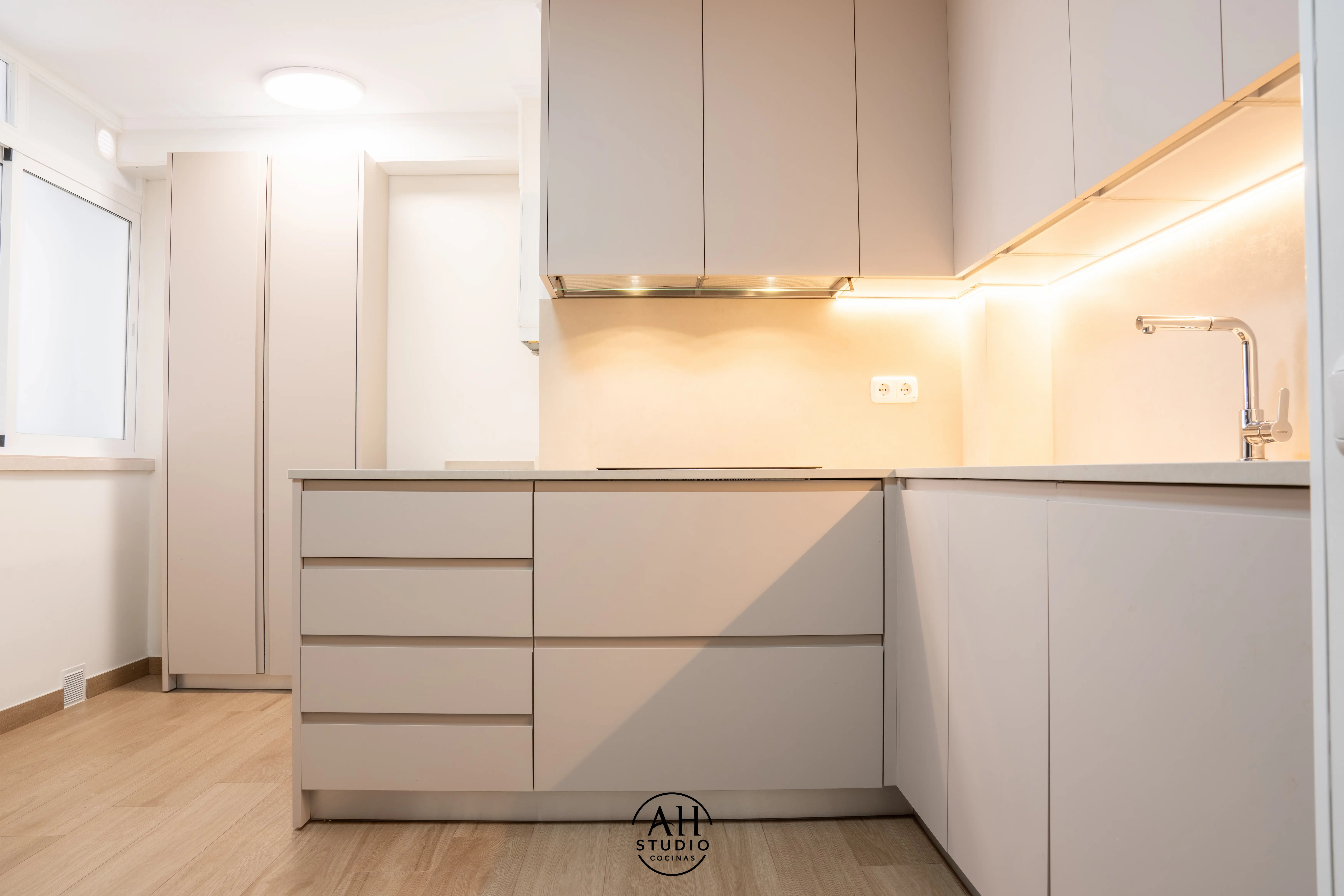 Cocina beige en L sin tiradores con luz cálida bajo los muebles altos