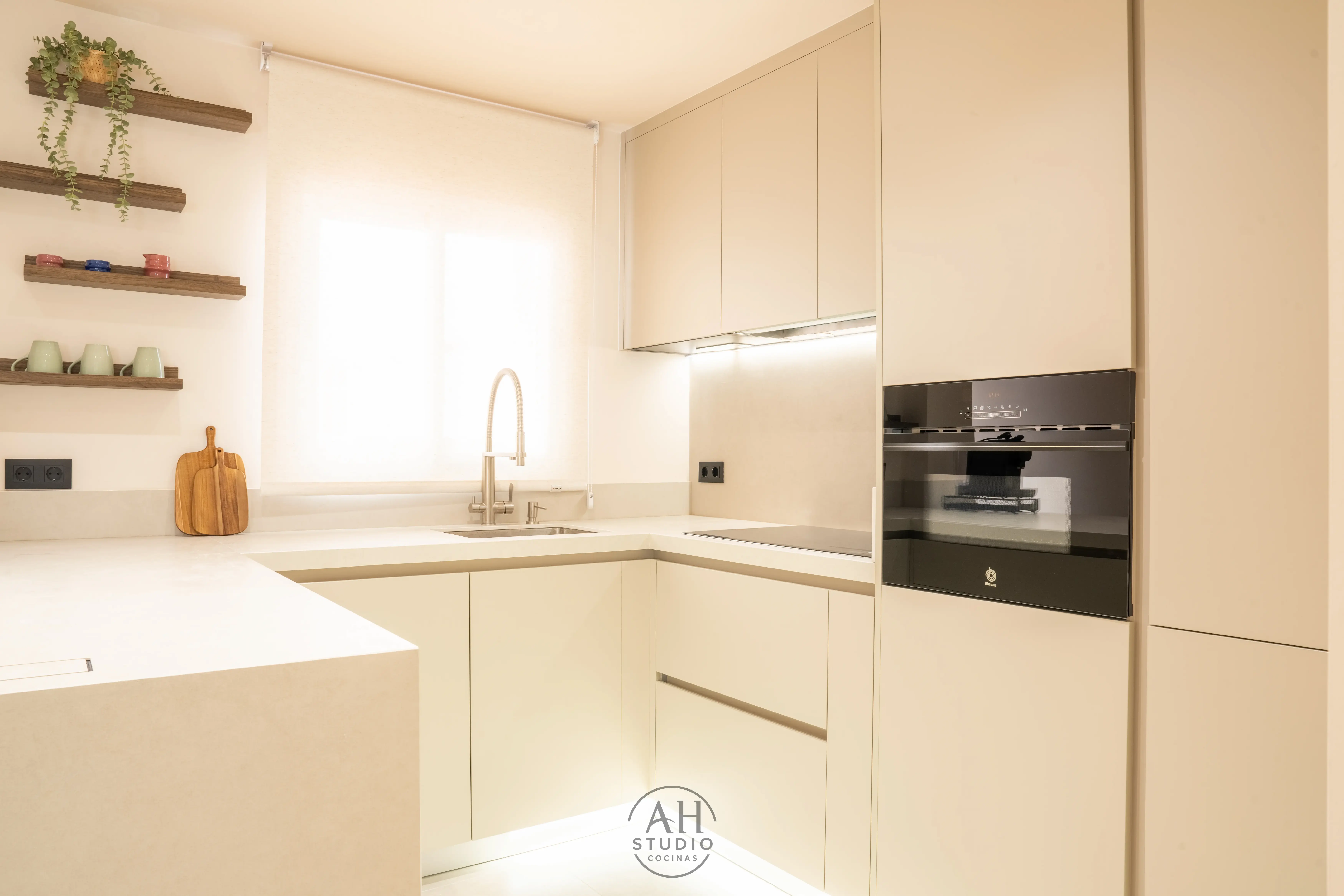 Cocina en U color crema con horno compacto negro, ventana y baldas de madera