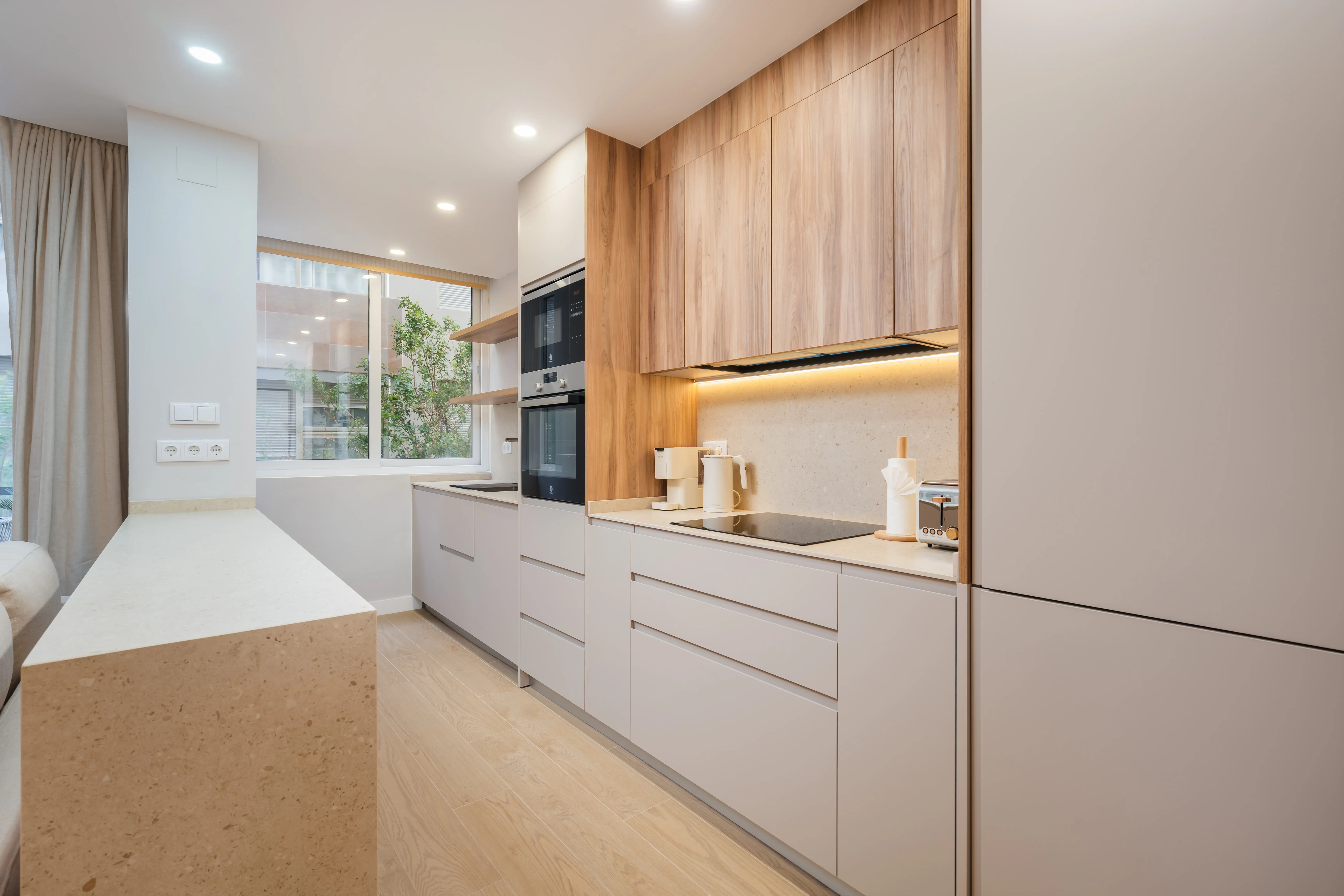 Cocina en galería con muebles altos de madera, bajos beige y encimera de terrazo